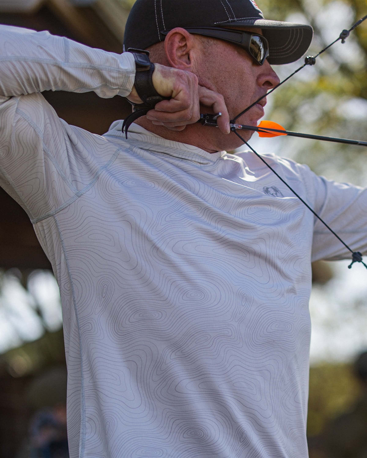 Man with drawn compound bow wearing the Gila LS Hoodie in Skyline White Topo Print