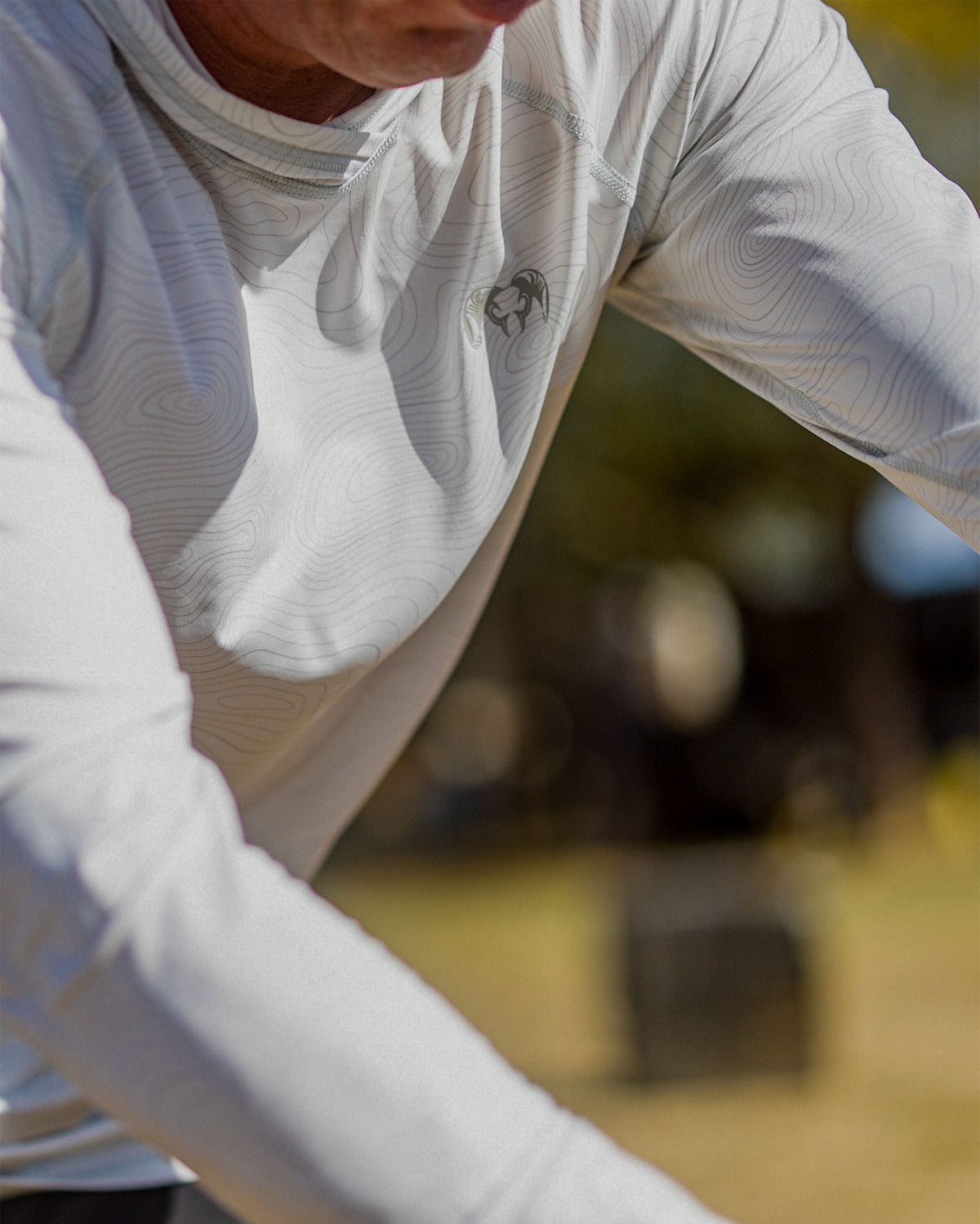 Detail of man with outstretched arms focused on collar and small chest ram logo wearing the Gila LS Hoodie in Skyline White Topo Print
