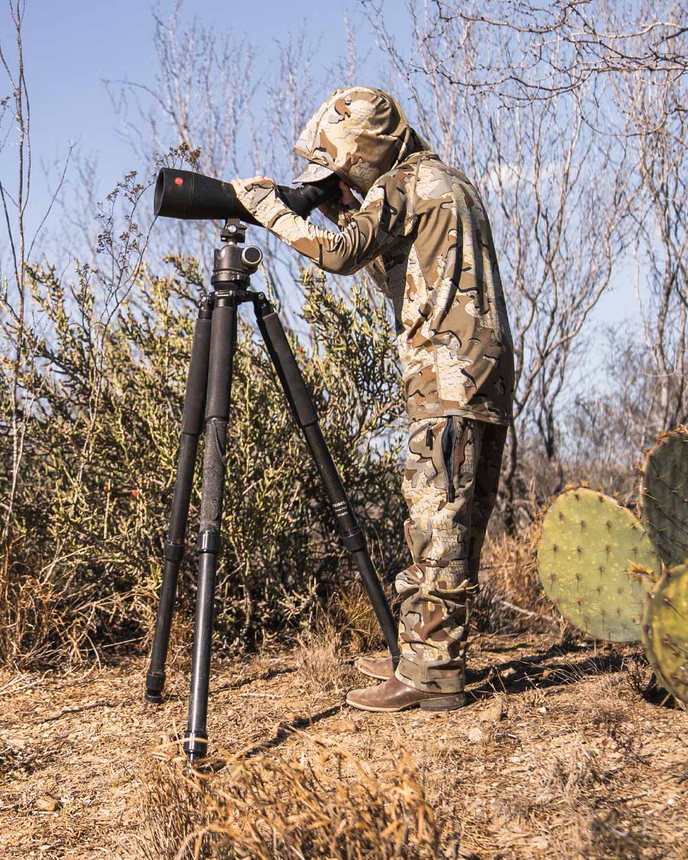 Youth hunter standing, wearing Youth Gila LS Hoodie in Valo Camouflage, glassing using a spotting scope