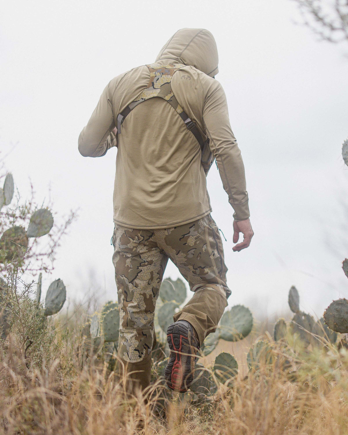 Back of hunter walking amongst cacti wearing the Gila PRO LS Hoodie in Khaki with hood on