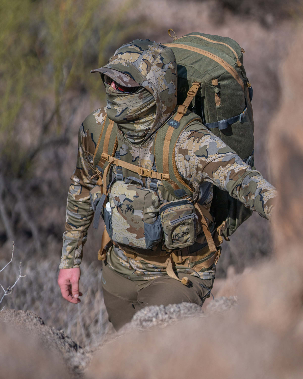 Hunter Looking Uphill in Gila Pro Long Sleeve Hoodie in Valo Camouflage Highlighting Built-in Neck Gaiter and Hood with Cap Capabilites