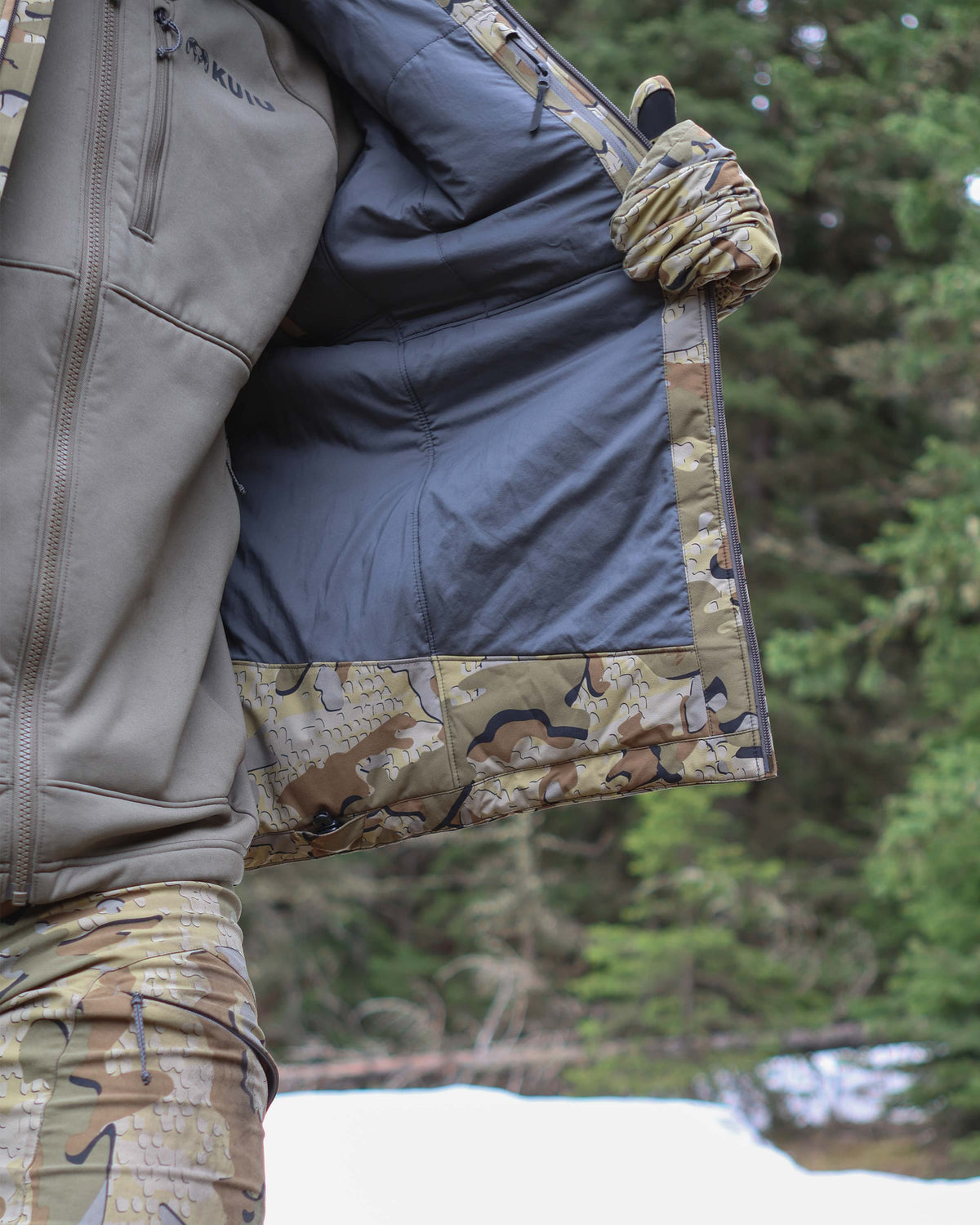 Hunter displaying extended bottom hem material and the adjustable hem cinch cord on Mountain PRO Hooded Jacket in Valo Camouflage
