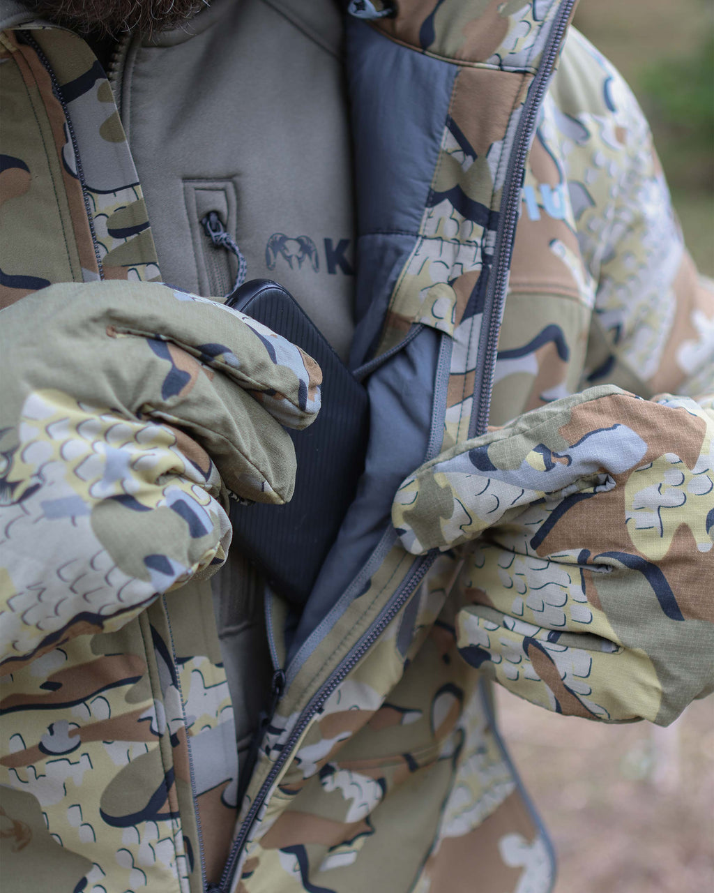 Hunter stowing a cell phone in internal zippered pocket of Mountain PRO Hooded Jacket in Valo Camouflage