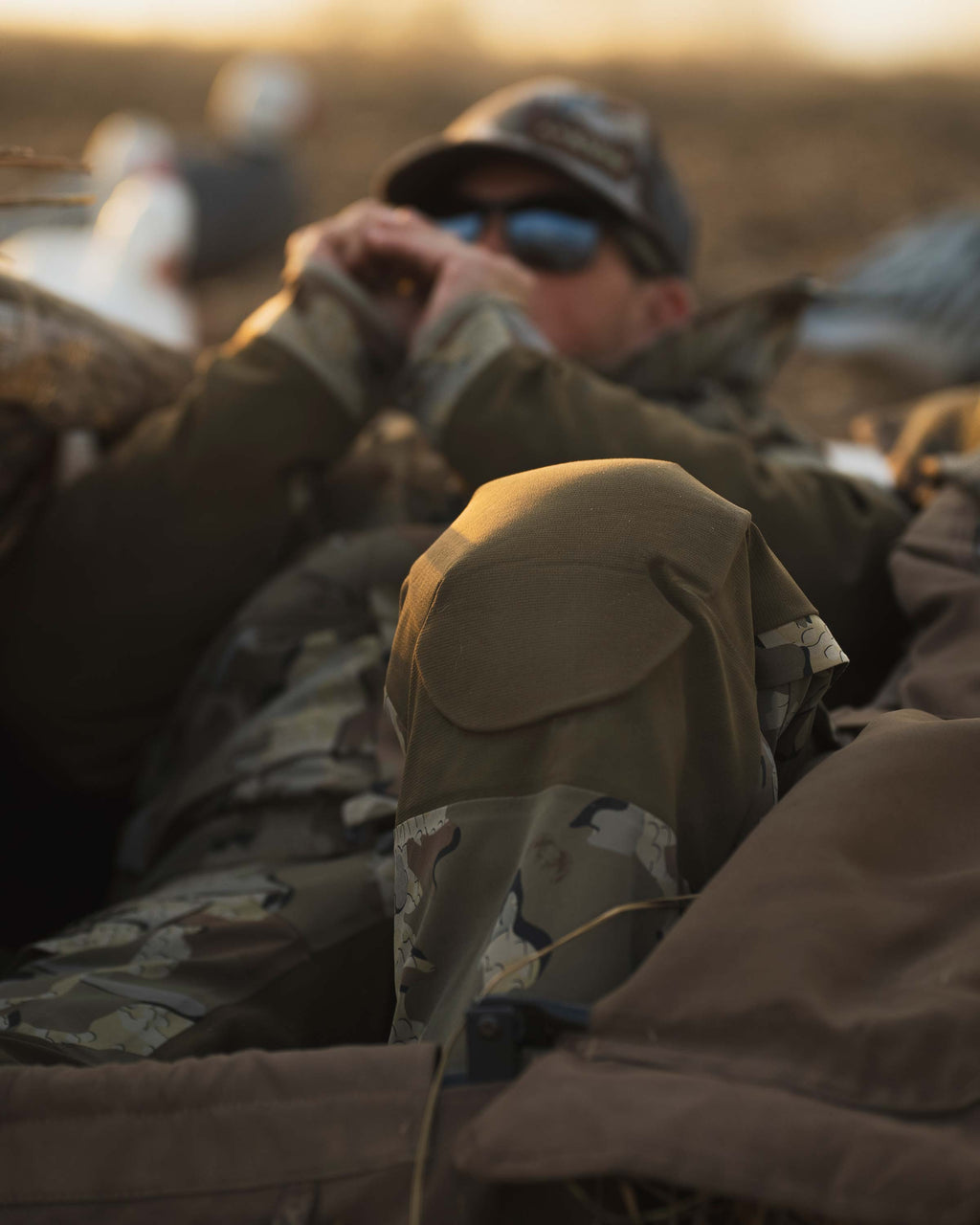 Waterfowl hunter in layout field blind wearing KUIU Paragon Storm Shell Parka and Bib in Valo Camouflage