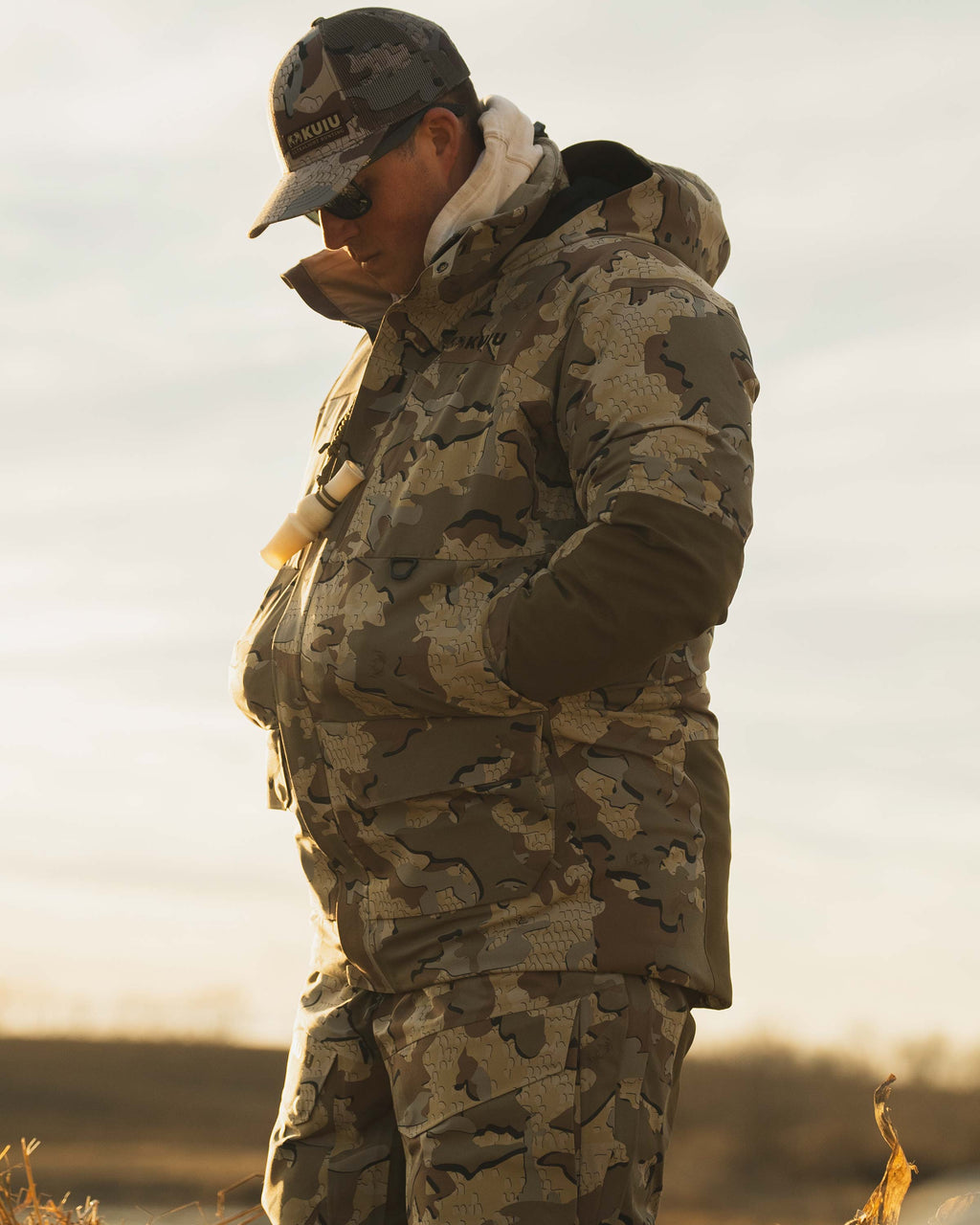 Side view of Waterfowl Hunter wearing Paragon Storm Shell Parka and Bib in Valo Camouflage, with his hands in his pockets