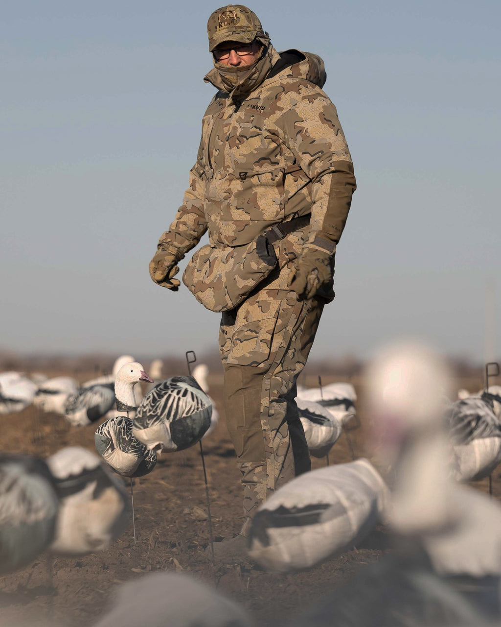Waterfowl Hunter wearing Paragon Storm Shell Parka, Bib and Hand Muff in Valo Camouflage standing in the middle of a field with snow goose decoys