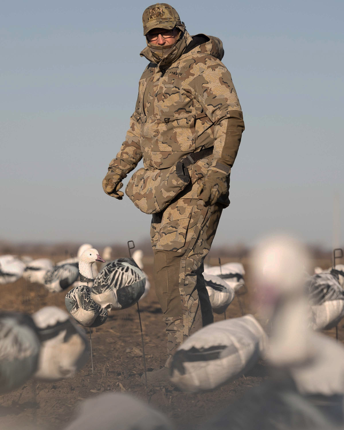 Waterfowl Hunter wearing Paragon Storm Shell Parka, Bib and Hand Muff in Valo Camouflage standing in the middle of a field with snow goose decoys