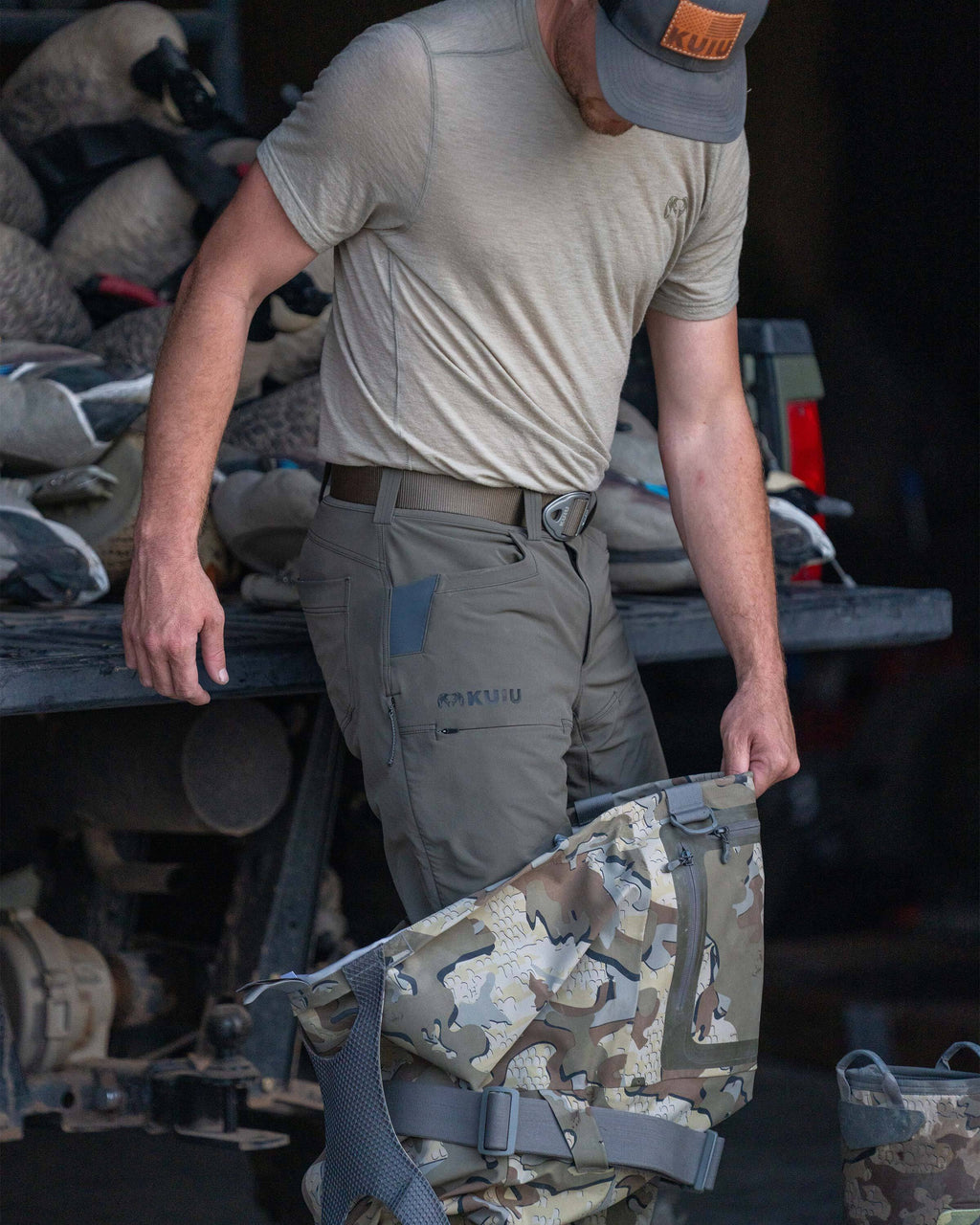 Hunter in front of a truck filled with duck decoys, wearing Reed Pant in Ash Brown while stepping into KUIU HD Flex Wader in Valo Camouflage