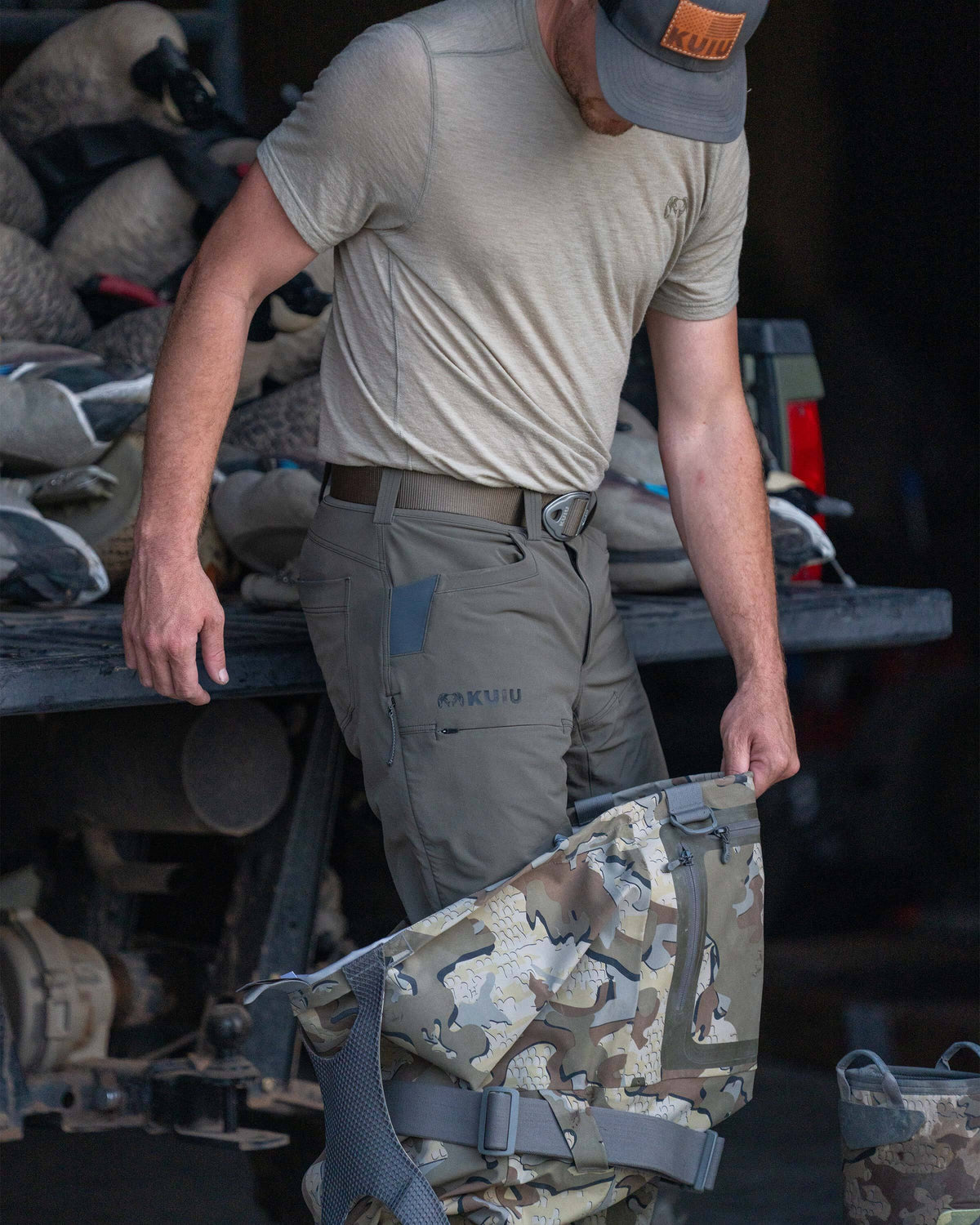 Hunter in front of a truck filled with duck decoys, wearing Reed Pant in Ash Brown while stepping into KUIU HD Flex Wader in Valo Camouflage
