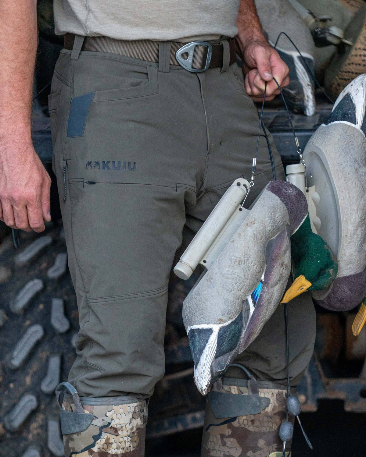 Close-up of hunter wearing Reed Pant in Ash Brown, carrying a couple of duck decoys in his left hand
