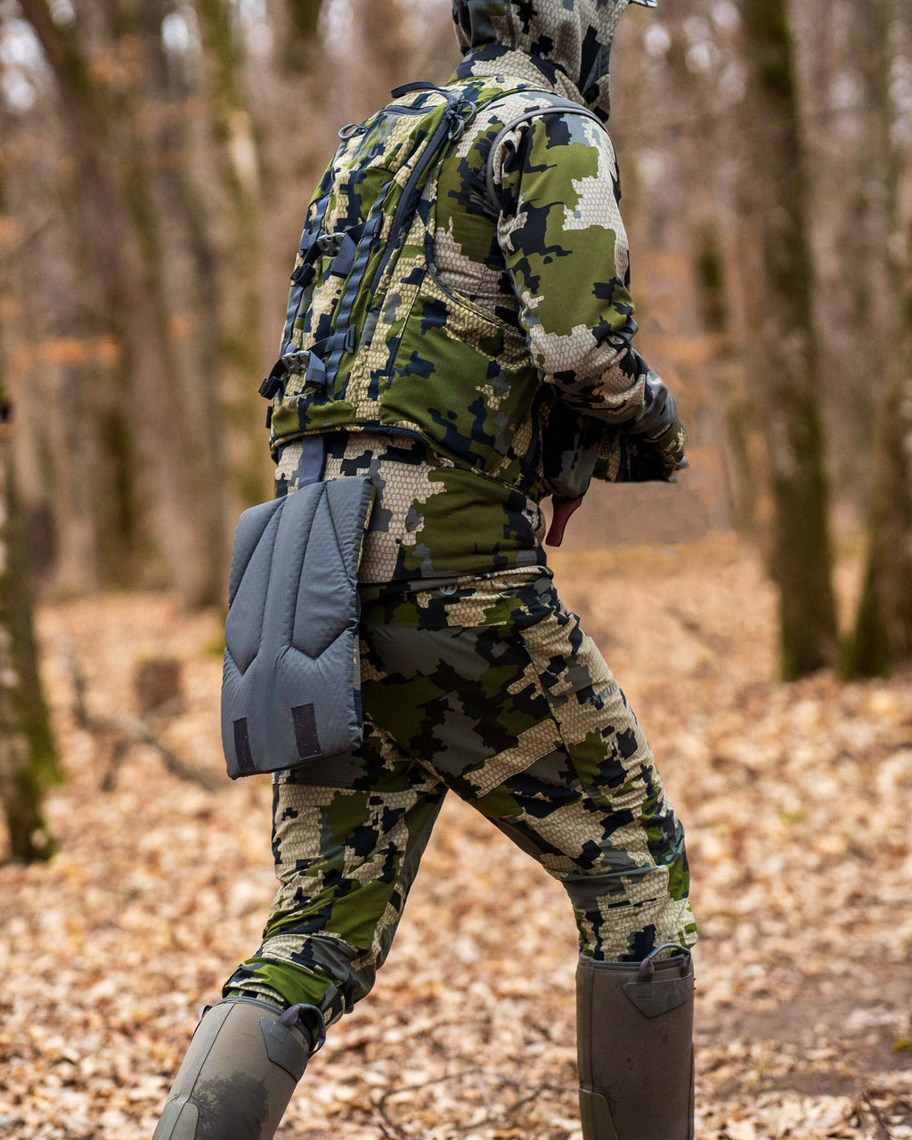 Hunter walking through the woods wearing Kutana Hybrid Pant in Verde Camouflage andthe Rival Turkey Vest with BackTrack™ deployable seat shown in  Verde Camouflage