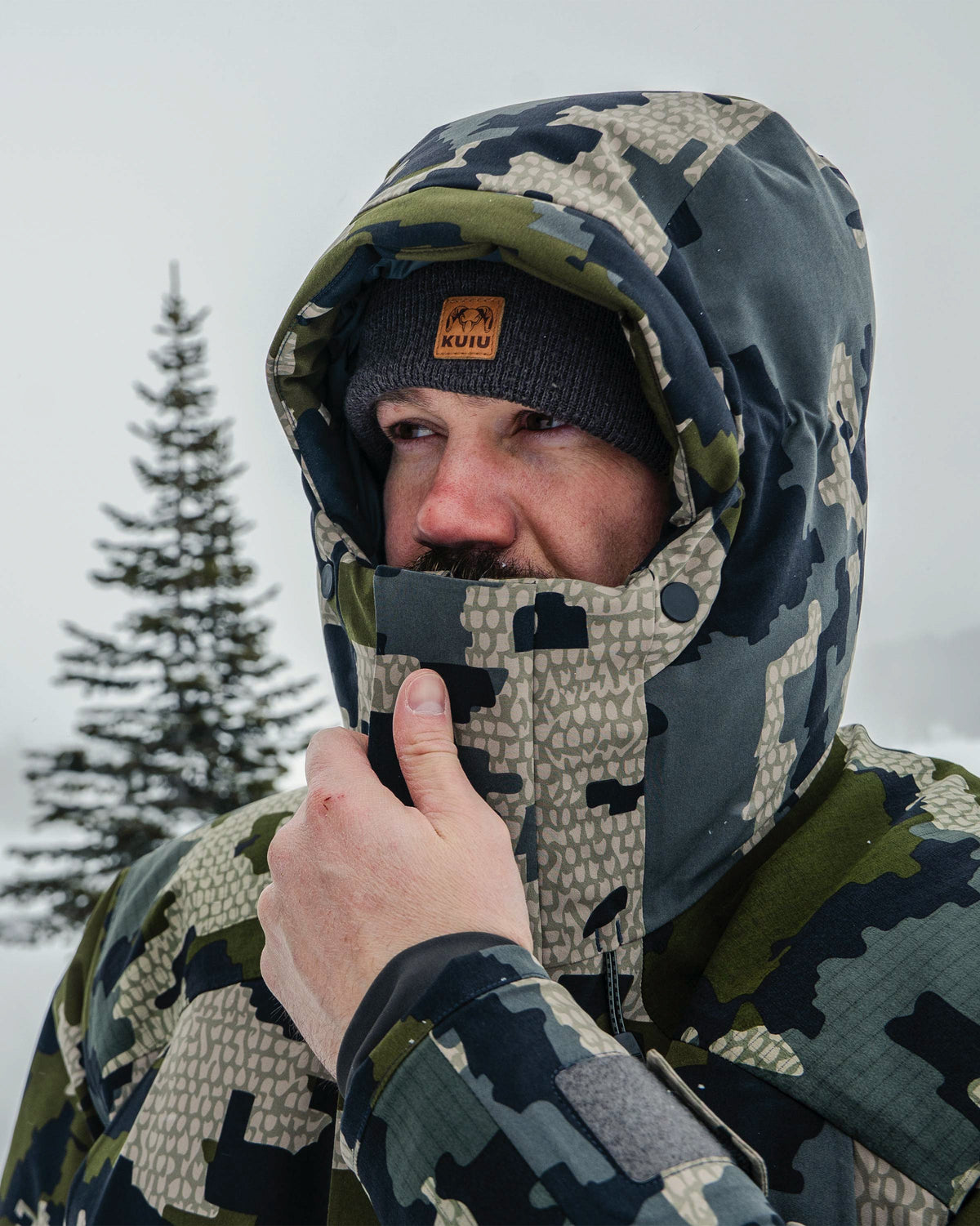 Hunter in a cold outdoor setting wearing Super Down Arktuk Parka in Asphalt Grey, holding the top chin guard