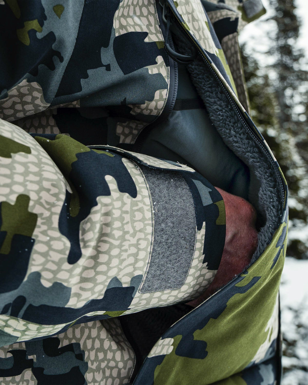 Close-up of hunter's hand warming in a sherpa fleece pocket on the Super Down Arktuk Parka in Verde Camouflage