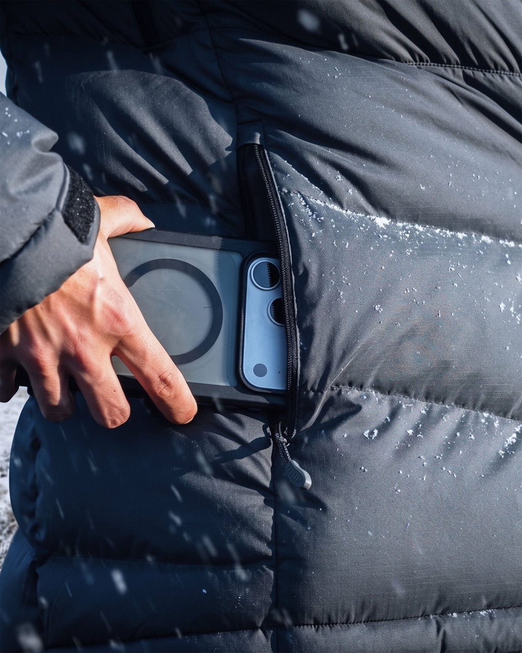 A close-up of a Women's Super Down PRO Jacket with a hand reaching into a side pocket to retrieve a smartphone with snowflakes visible on the jacket.