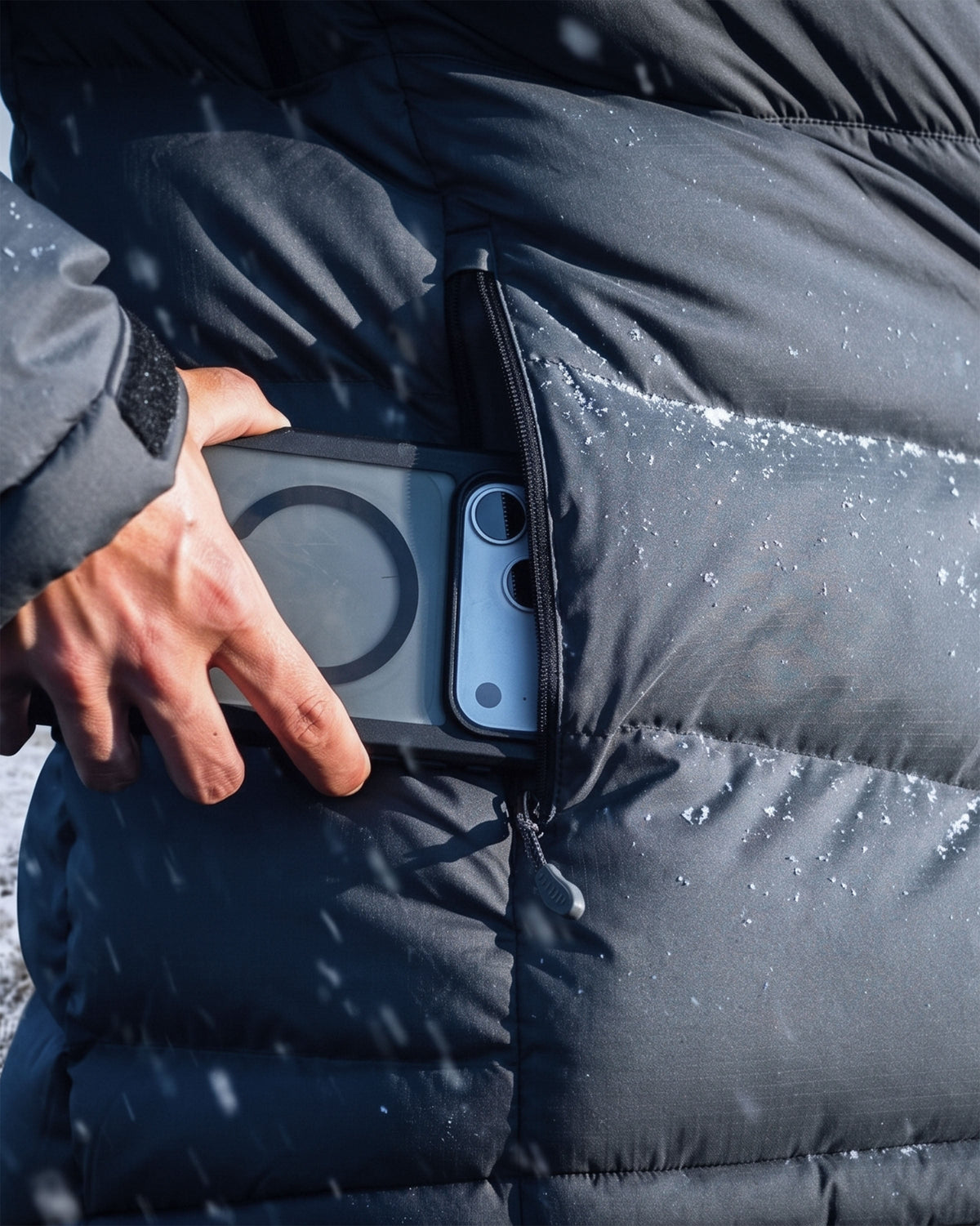 A close-up of a Women's Super Down PRO Jacket with a hand reaching into a side pocket to retrieve a smartphone with snowflakes visible on the jacket.