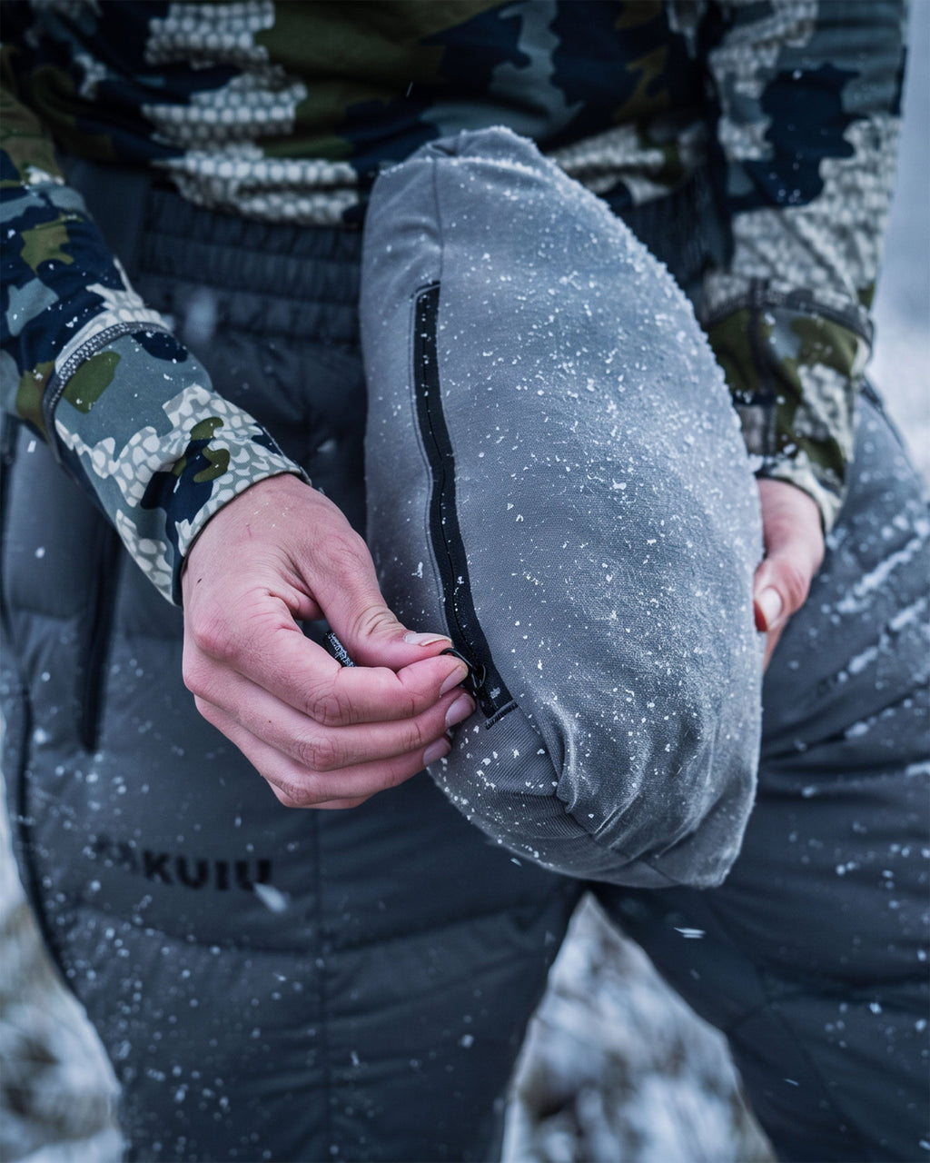 A person outdoors in a snowy landscape displaying packable feature on the Women's Super Down PRO Jacket in Gunmetal Grey.