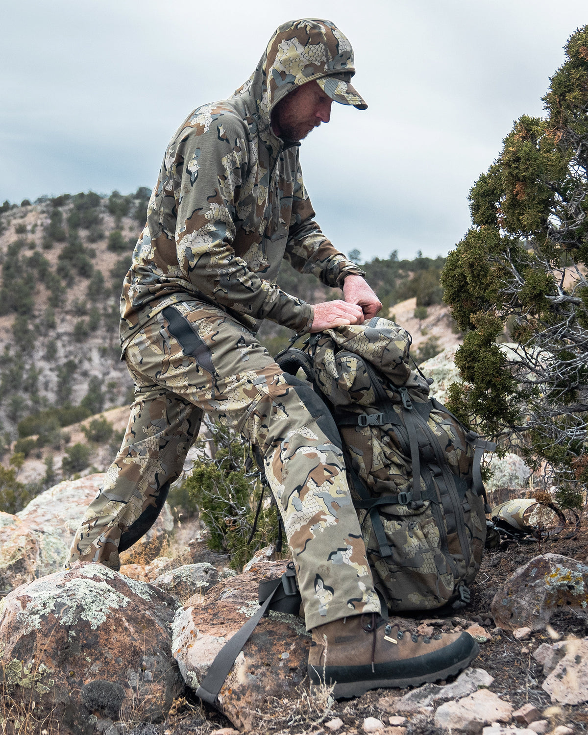 Hunter wearing PRO Pant in Valo Camouflage with hip vents open while loading gear into a backpack
