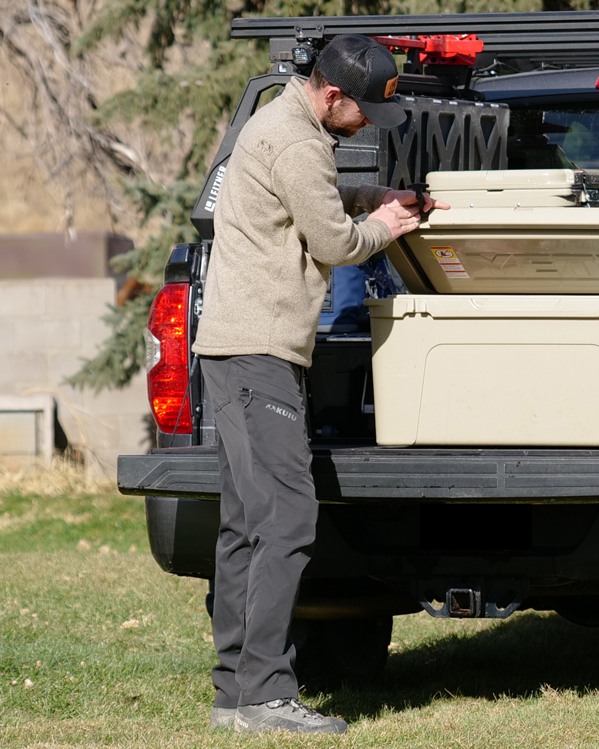 Man wearing the Base Camp Sierra Pant in Gunmetal, closing a cooler in his truck bed