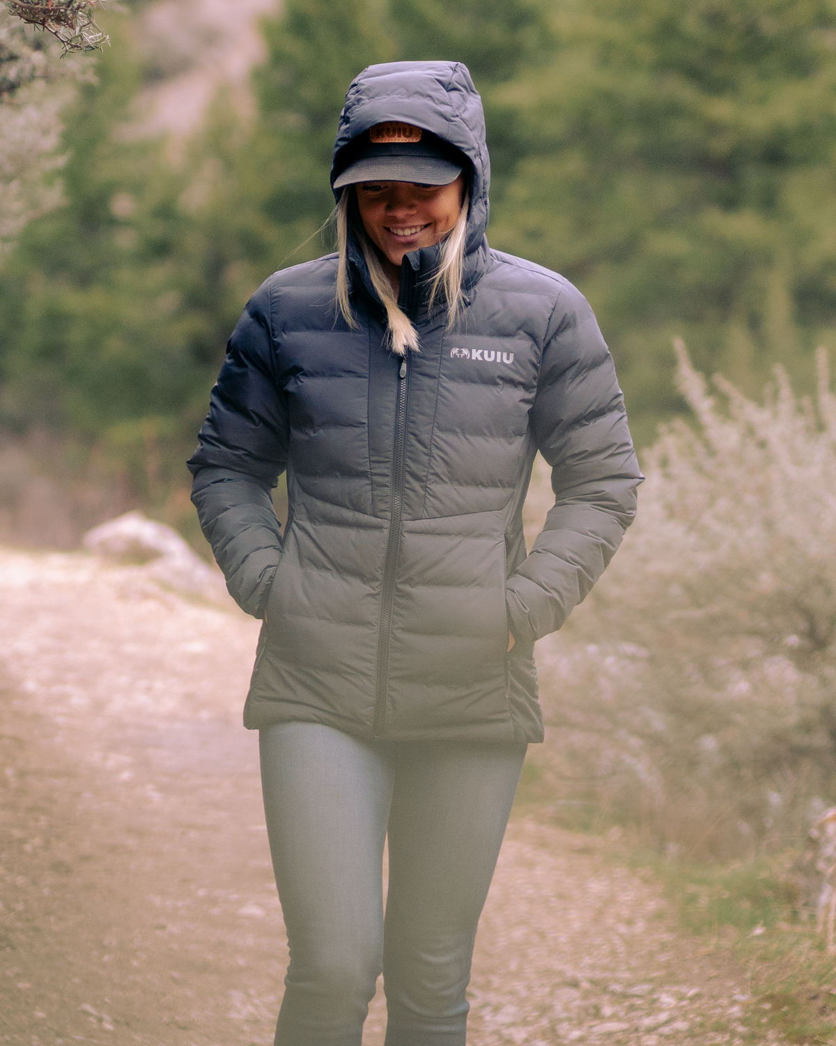 Woman wearing Elements Hooded Jacket in Gunmetal with hood on and hands inside zippered hand pockets